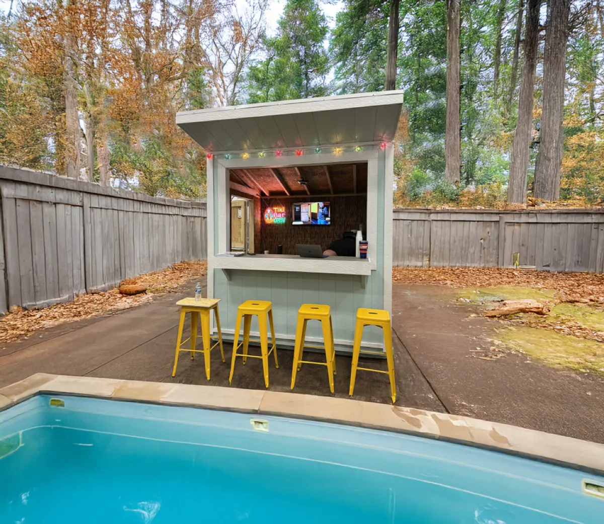 Backyard bar building with a serving window, string lights and four stools