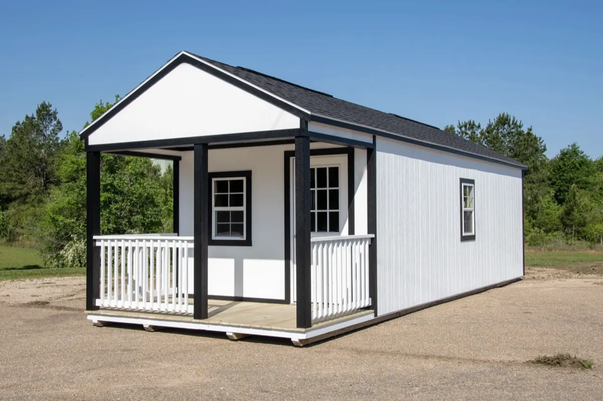 White cabin with black trim and a covered front porch with white railing