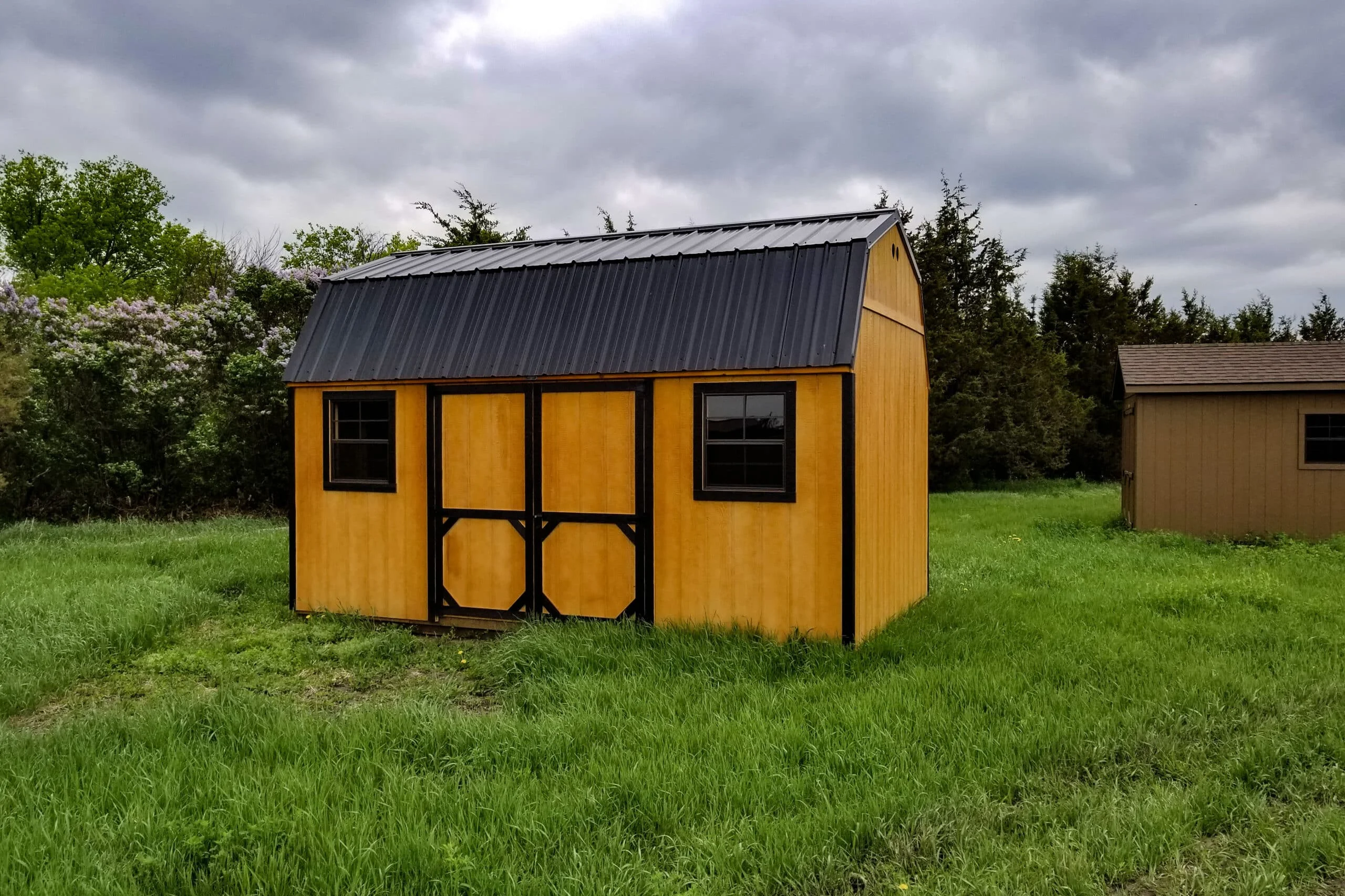 Tan lofted barn with dark trim and a charcoal metal roof under a cloudy sky