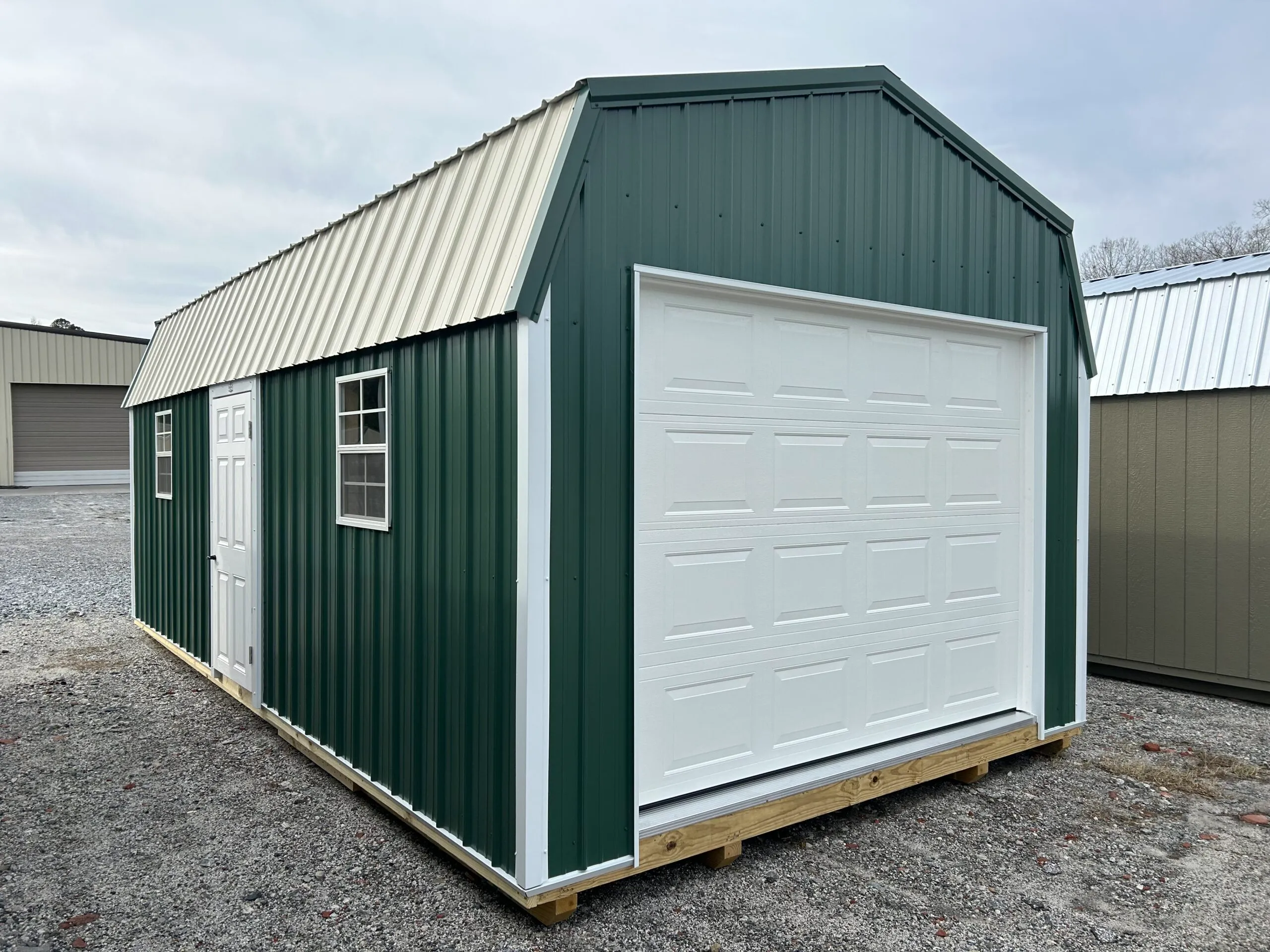 Dark green portable garage with a white roll-up door and a walk-in side entry on a gravel lot