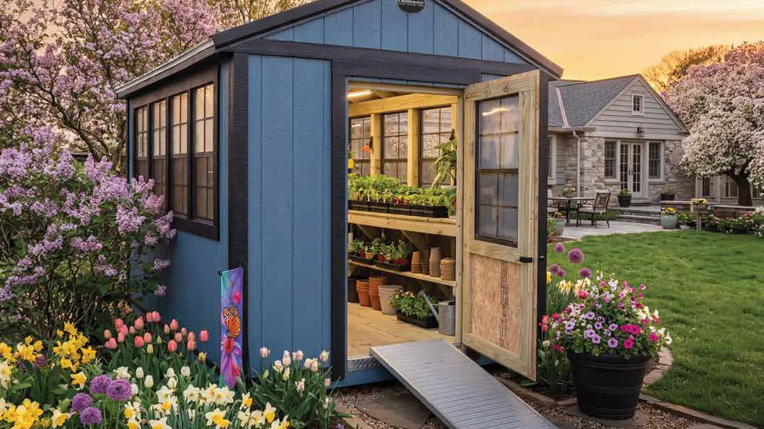 Blue garden shed with open doors beside a flower garden at sunset