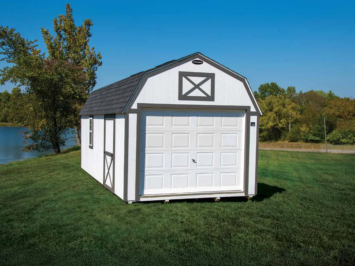 White lofted portable garage with a roll-up door beside a lake